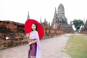 Beautiful Thai girl in traditional dress costume red umbrella as Thai temple where is the public place, Thai Woman in Traditional Costume of Thailand. photo