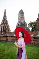 Beautiful Thai girl in traditional dress costume red umbrella as Thai temple where is the public place, Thai Woman in Traditional Costume of Thailand. photo