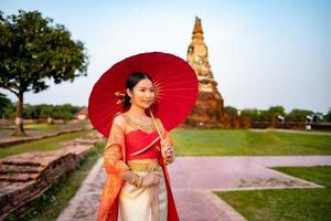 hermosa tailandés niña en tradicional vestir disfraz rojo paraguas como tailandés templo dónde es el público lugar, tailandés mujer en tradicional disfraz de tailandia foto