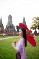 hermosa tailandés niña en tradicional vestir disfraz rojo paraguas como tailandés templo dónde es el público lugar, tailandés mujer en tradicional disfraz de tailandia foto