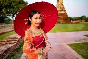 hermosa tailandés niña en tradicional vestir disfraz rojo paraguas como tailandés templo dónde es el público lugar, tailandés mujer en tradicional disfraz de tailandia foto