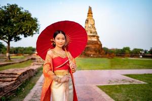 hermosa tailandés niña en tradicional vestir disfraz rojo paraguas como tailandés templo dónde es el público lugar, tailandés mujer en tradicional disfraz de tailandia foto