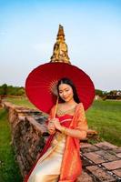 Beautiful Thai girl in traditional dress costume red umbrella as Thai temple where is the public place, Thai Woman in Traditional Costume of Thailand. photo