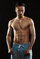 Portrait of a shirtless confident young athletic man standing against black photo