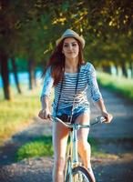 encantador joven mujer en un sombrero montando un bicicleta al aire libre. activo personas foto