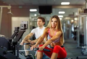 Athletic man and woman training on row machine in gym photo