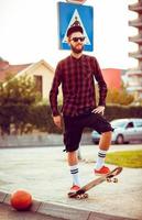 Young man in sunglasses with a skateboard on a street in the city at sunset light photo