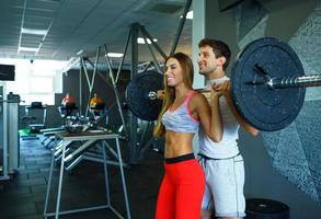 atlético hombre y mujer con barra con pesas haciendo ejercicios en el gimnasio foto