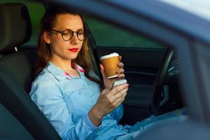 mujer de negocios enviando un texto mensaje y Bebiendo café mientras conducción un coche foto