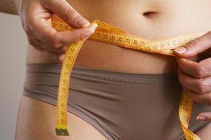 Woman measures a waist with a centimeter ribbon photo