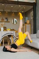 joven hermosa mujer en ropa de deporte lo hace un aptitud rutina de ejercicio a hogar, levantamiento su piernas arriba foto