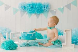 Birthday party for a one-year-old boy in blue and turquoise garlands and a cake, holiday concept and decor, a child with a cake