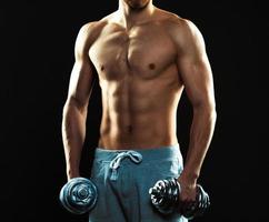 Athletic attractive man with dumbbells on the black photo