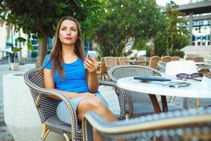 Young pretty woman relaxing in the outdoor cafe and using smartphone photo