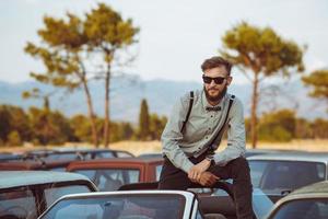 joven hermoso elegante hombre, vistiendo camisa y corbata de moño en el campo de antiguo carros foto