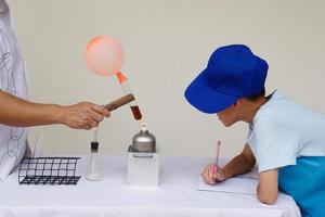 estudiante es observando, tomando Nota acerca de el reacción de globo en prueba tubo es quemado desde linterna. concepto, Ciencias experimento. el en expansión de aire presión y agua hirviendo. foto