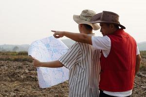 Asian father and son are exploring and surveying their own land, father points to boundary, son holds map. Concept, land property planning, legacy.Exploration. photo