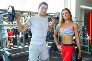 atlético hombre y mujer con barra con pesas haciendo ejercicios en el gimnasio foto