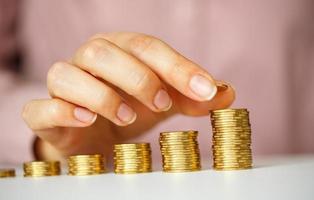Female hand stacking gold coins into increasing columns photo
