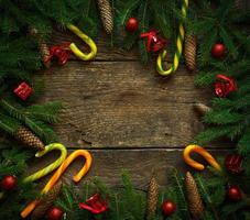 Borde de Navidad con ramas de abeto, conos, adornos navideños y bastón de caramelo sobre tablas de madera rústica foto