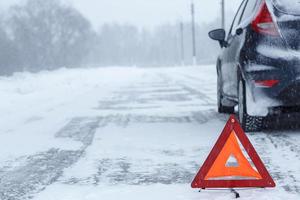 Closeup of red warning triangle with a broken down car in winter photo