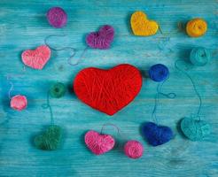 Multicolored Hearts with a balls of thread on blue wooden background photo