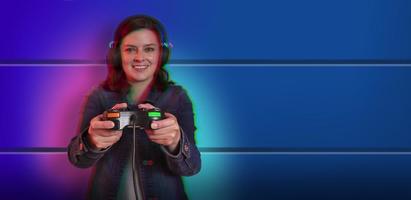 Beautiful young hispanic woman standing front view playing with a video game console in her hands against blue wall background. focus on hands photo