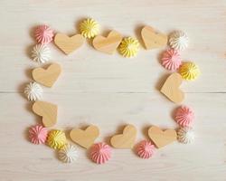 Frame made of wooden hearts and meringue pastel colors on a white wooden background photo