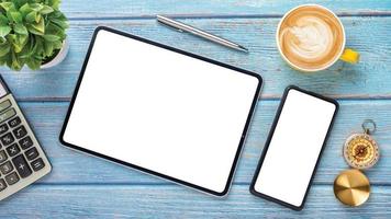 Wooden desk workplace with blank screen tablet and smart phone, pen, calculator and cup of coffee, Top view flat lay. photo