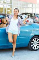 Young happy woman standing near a convertible with the keys in his hand and thumb up photo