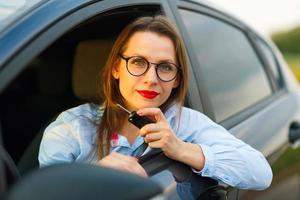 joven bonito mujer sentado en un coche con el llaves en mano foto