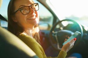 Woman in glasses uses a smartphone while driving a car at sunset photo