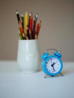 pequeño azul alarma reloj y un vaso con de colores lapices en un mesa foto