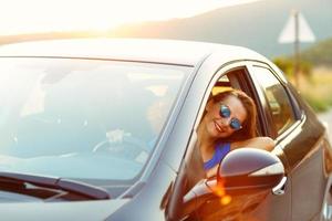 sonriente mujer conducción un coche a puesta de sol foto