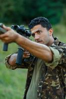 Man of Arab nationality in camouflage with a gun aiming at a target photo