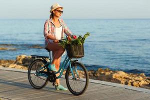 Carefree woman with bicycle riding on a wooden path at the sea, having fun and smiling photo