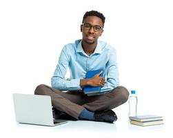 Happy african american college student with laptop, books and bottle of water sitting on white photo