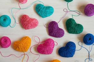 Multicolored Hearts with a balls of thread on white wooden background photo