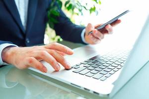 Men office worker typing on the keyboard and using smartphone photo