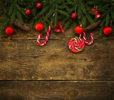 Borde de Navidad con ramas de abeto, conos, adornos navideños y bastón de caramelo sobre tablas de madera rústica foto