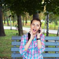 A portrait of a smiling woman in a park on a bench talking on the phone photo