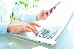 Hands or men office worker typing on the keyboard and using smartphone photo