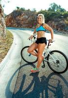 atlético mujer en pie cerca su bicicleta en un montaña la carretera foto