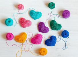 Multicolored Hearts with a balls of thread on white wooden background photo