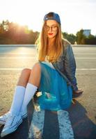 al aire libre Moda de cerca verano retrato de bonito joven mujer posando con patineta en urbano juventud estilo en ciudad. verano noche luz de sol foto