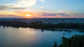 volador terminado el arboles y lago en el ciudad a amanecer - aéreo foto