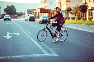 joven hombre en Gafas de sol montando un bicicleta en ciudad calle foto