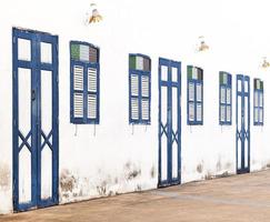 Blue wooden door and window pattern row on old white wall background photo