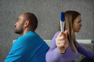 A man and a woman are sitting on the bed with their backs to each other, they are upset in the hands of a woman a negative pregnancy test, difficulties with pregnancy photo