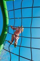 Happy little active girl climbed on a rope web on a playground against a bright blue sky on a sunny day photo